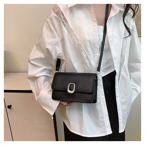 Detail of a black square leather crossbody bag with silver oval clasp on a model
