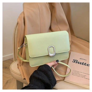 Close-up of mint green rectangular bag with silver textured buckle on a beige suit background