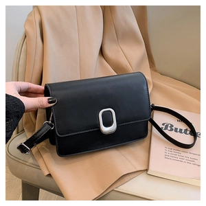 Close-up of black leather square bag with silver oval buckle on beige blazer