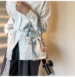 Detail of cream bucket bag with blue woven handle and pink charm on stairs