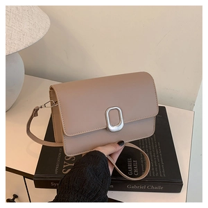 Detail of light khaki square bag with metallic buckle on a minimalist book background