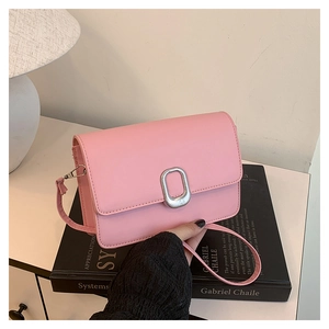 Detail of pink faux leather crossbody bag featuring an oval silver metal buckle on the flap