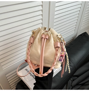 Detail of cream drawstring bucket bag featuring a pink woven handle and cute charm