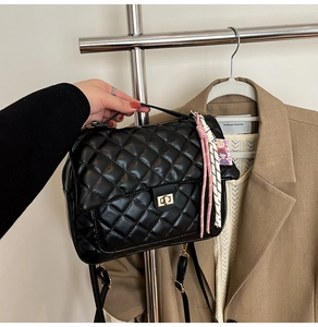 Detail of black quilted tote bag with gold square twist lock and woven charm