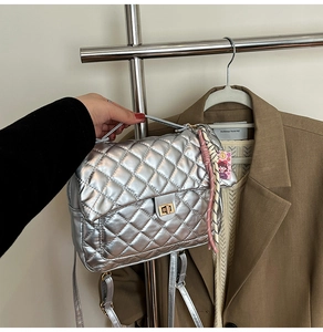 Quilted silver tote bag detail with gold lock and decorative charm on brown blazer