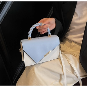 Detail of light blue and white color-block crossbody bag with woven handle and metal trim