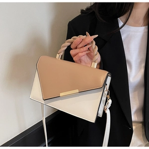 Detail of a color-block handbag showing the twisted top handle and gold metal lock clasp