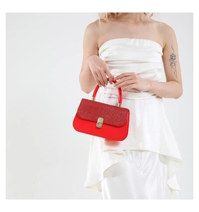 Detail of red sequined handbag with gold clasp held by a model in a white dress