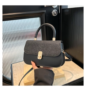 Detail of glitter texture and golden metal twist lock on black leather crossbody bag
