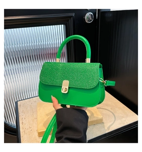 Close-up of vibrant green handbag featuring a glitter flap and gold twist-lock closure