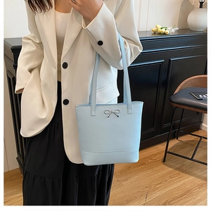 Gros plan d'un sac cabas bleu clair avec un nœud argenté porté avec un blazer blanc
