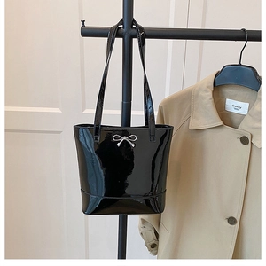Détail d'un sac cabas en cuir verni noir avec nœud argenté et finition brillante