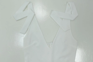 Detail of white V-neck dress featuring elegant ribbon shoulder straps and smooth fabric
