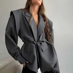 Detail of grey V-neck blazer showing structural padded shoulders and waist tie texture