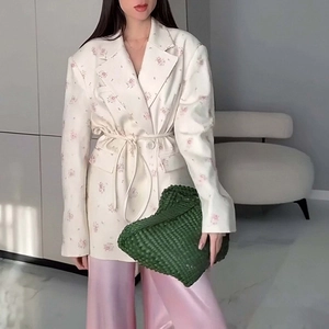 Detail of floral blazer with waist belt and pink satin trousers on fashion model