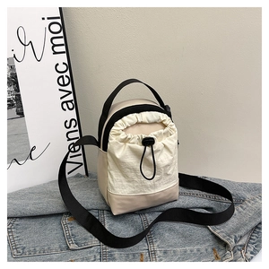 Detail of beige drawstring crossbody bag with black nylon straps on denim jacket