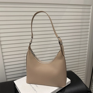 Beige minimalist crescent shoulder bag with silver hardware and adjustable strap on a book