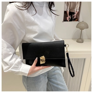 Detail of black pleated envelope clutch featuring a gold geometric metal clasp and wristlet