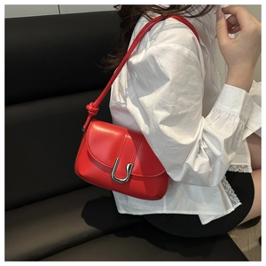 Detail shot of a bright red crossbody bag with silver U-shaped clasp on a white shirt