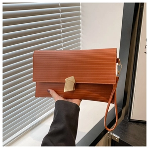 Detail of caramel envelope clutch bag featuring horizontal textures and gold buckle