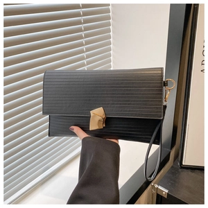 Detail of black textured envelope clutch with gold geometric clasp and wrist strap