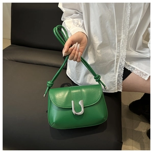 Detail of green leather crossbody bag with silver U-shaped buckle and knot strap design