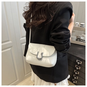 Detail of ivory faux leather crossbody bag with a large silver U-shaped metal buckle