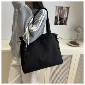 Detail view of large black nylon tote bag featuring side drawstrings on model