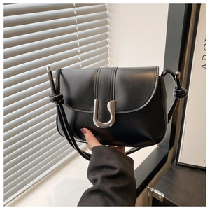 Detail of minimalist black leather crossbody bag with silver U-shaped clasp and knotted straps