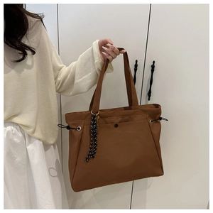 Detail of brown tote bag with drawstring side and black-white striped charm accessory