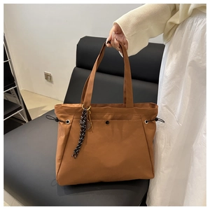 Detail of dark brown tote bag featuring adjustable side drawstrings and tennis charm