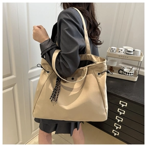 Detailed view of large khaki tote bag with drawstring side and stylish fringe charm