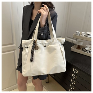 Detail of a beige tote bag featuring side drawstrings and a badminton racket pendant