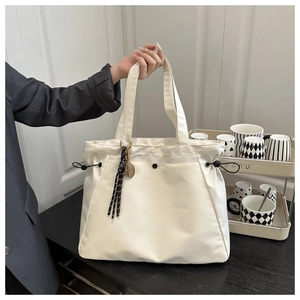 Detail of a large beige drawstring tote bag with striped tassel and metal ring