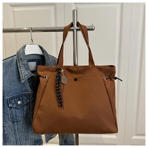 Detail of dark brown tote bag with gold tennis racket pendant hanging on a white door