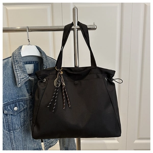 Detail of black nylon tote bag with drawstring sides and tennis racket charm accessory