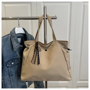 Detail view of large beige tote bag with side drawstrings and woven rope pendant