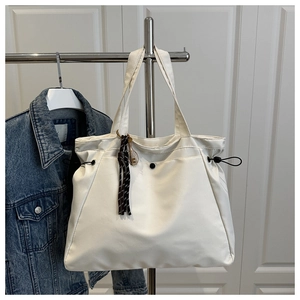 Detail of a large off-white nylon tote bag featuring a tennis racket charm and drawstring