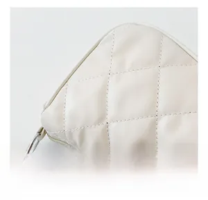 Close-up of diamond quilted stitching and silver metal chain on a beige shoulder bag