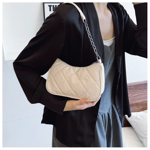 Detail of cream quilted shoulder bag with silver chain strap shown on model shoulder
