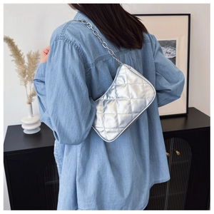 Close-up of a silver quilted shoulder bag with chain strap worn in a home setting