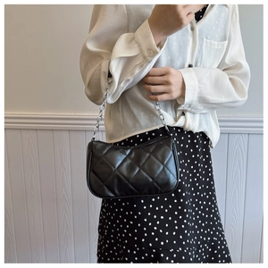Detail of black quilted leather shoulder bag with silver chain strap on a model
