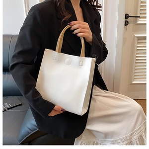 Detail of a white square tote bag with light brown handles and circular embossed logo