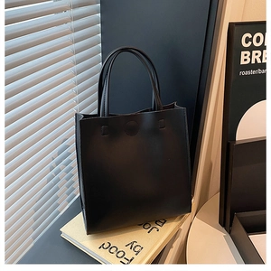 Detail of a minimalist black leather tote bag featuring a round magnetic clasp and dual handles