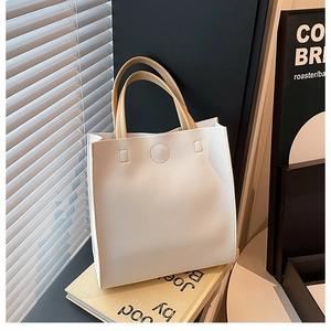 Detailed view of white faux leather tote bag with brown handles and magnetic snap closure