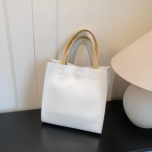 Minimalist white leather tote bag with khaki handles and circular embossed design on table