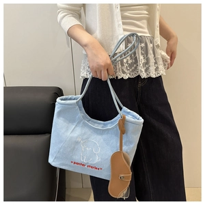 Close-up of light blue denim tote bag with cartoon dog embroidery and leather charm