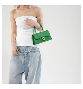 Detail of green handbag featuring glitter flap texture and gold circular twist lock