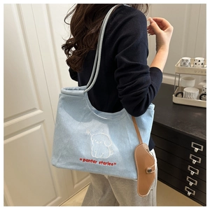 Detail of light blue denim tote bag with puppy embroidery and brown leather pendant