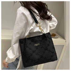 Close-up of black sequined tote bag with golden chain strap and brand metal logo